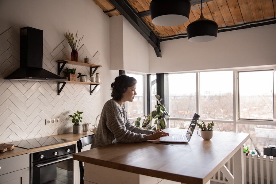 woman working on her laptop inside her home kitchen