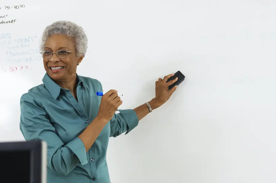 older african american professor in a blue shirt writing on a whiteboard