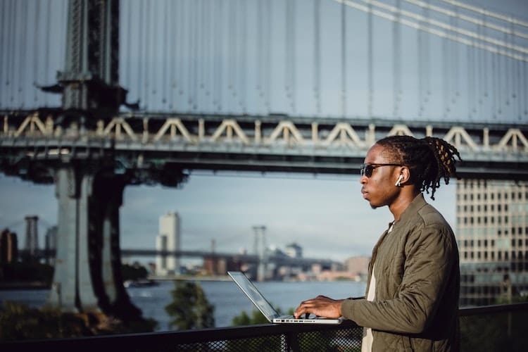 man with sunglasses working on his laptop next to the river in a big city