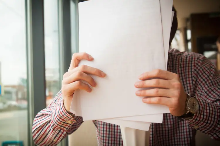 man holding a stack of notes in front of his face