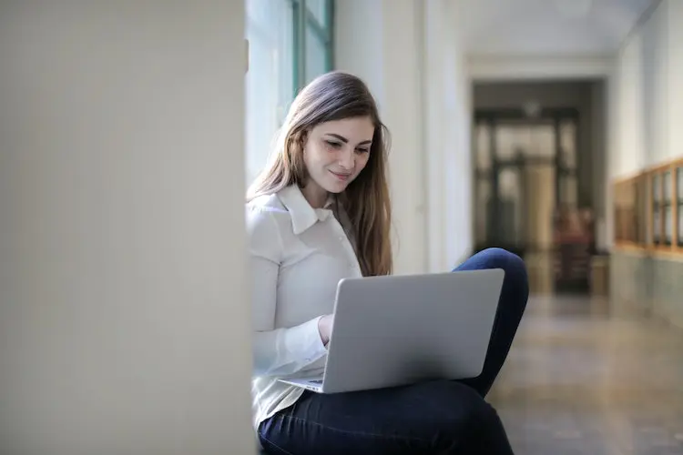 woman smiling and looking at her laptop in a college hall