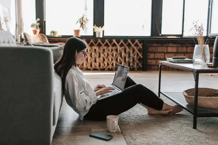 woman working on her laptop at home while sitting on the floor