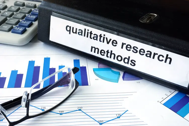 close up of a folder titled "qualitative research methods" and analytics charts next to it