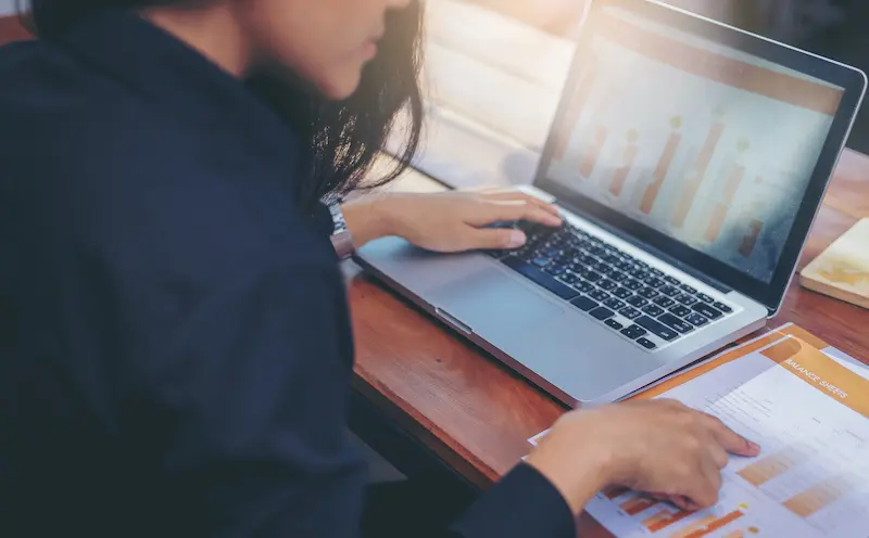 woman comparing charts between her notes and a laptop