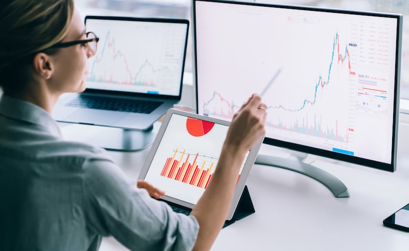 woman with eyeglasses comparing analytics charts on three screens