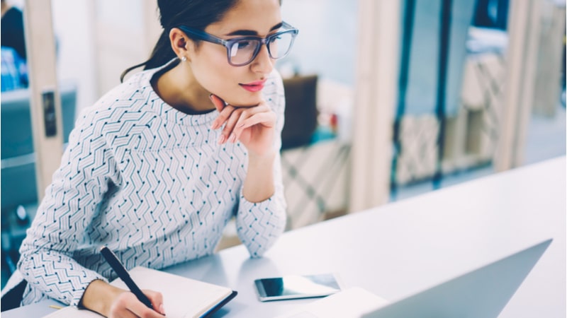 woman focused on writing notes next to her laptop