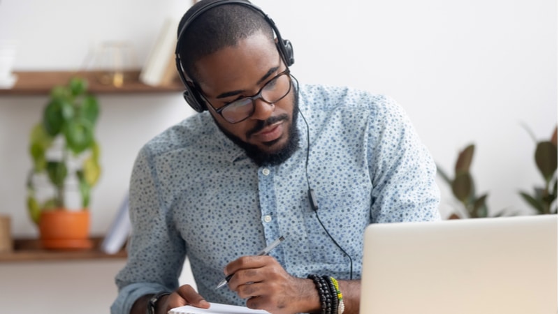 african american man with headphones taking notes from laptop