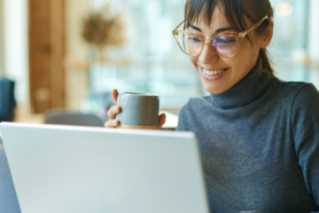 woman holding a cup of coffee and smiling at her laptop