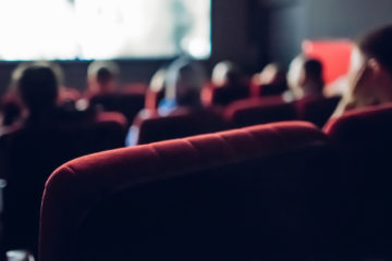 close up of a chair inside a movie theater with people in the background