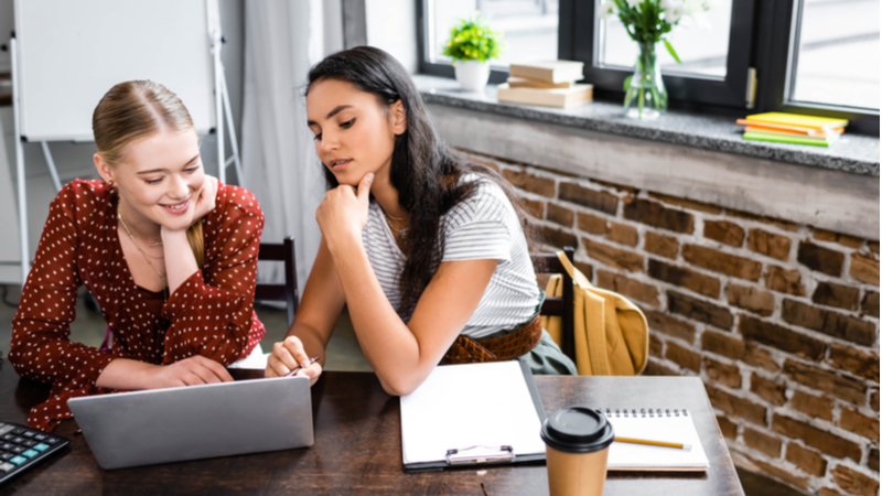 two women working together on a laptop in a modern office