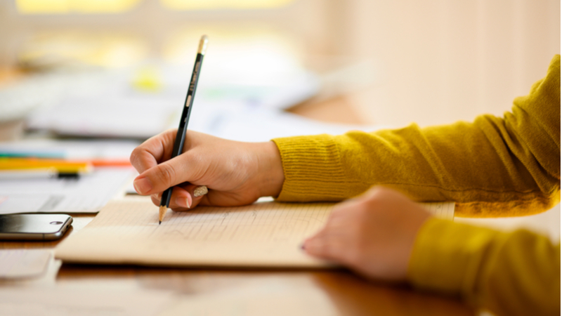 woman in yellow sweater using a pencil to take notes