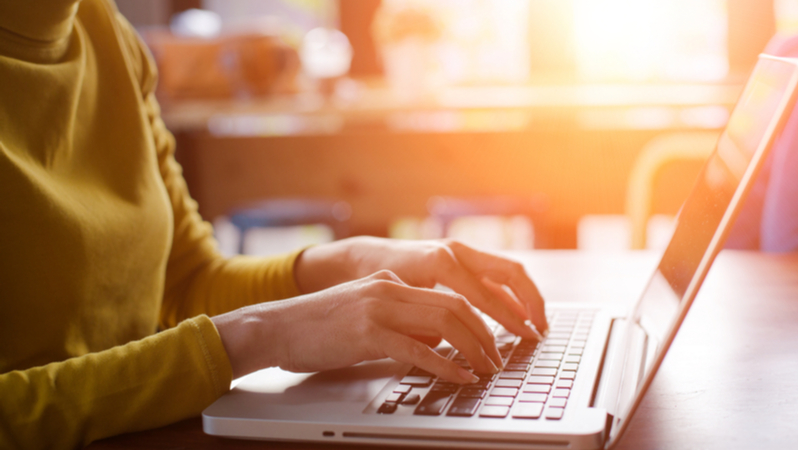 woman in a yellow sweater typing on a laptop