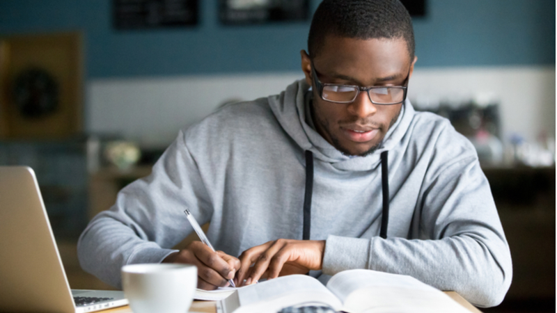 african american man in grey hoodie studying in front of his laptop