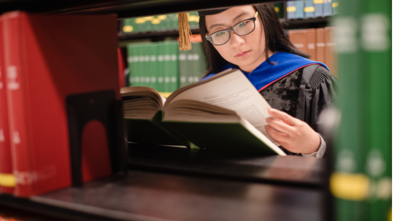 woman with glasses reading a book between library shelves