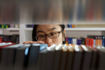 asian student looking through the library shelves
