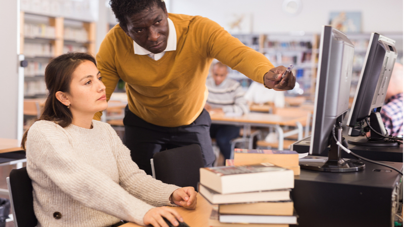 librarian in a yellow sweater helping a graduate student on the computer