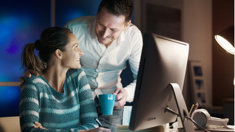 man bringing a cup of coffee to his girlfriend who is studying at the computer