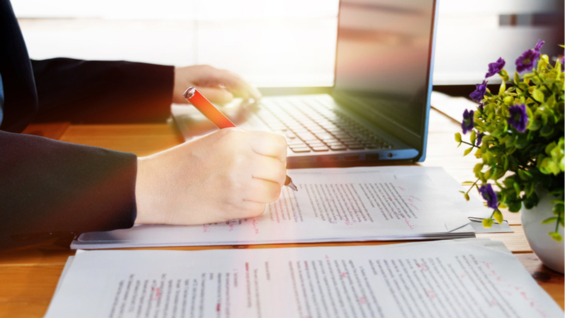 woman editing a paper with a red pen in front of her laptop