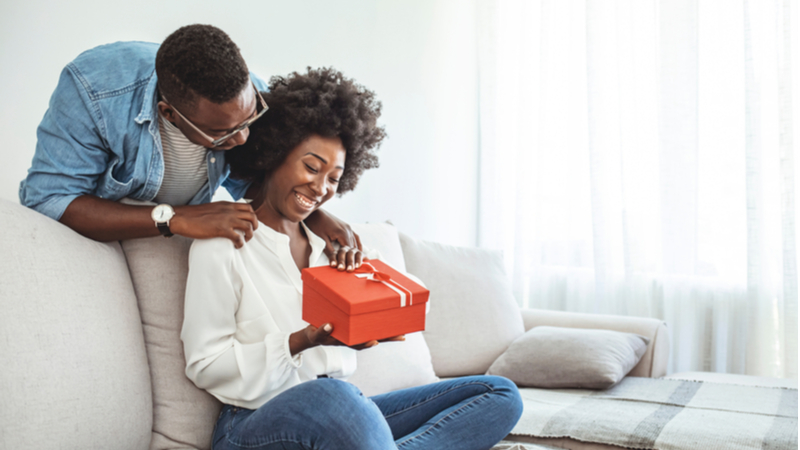 african american couple sitting on the couch and opening a gift box