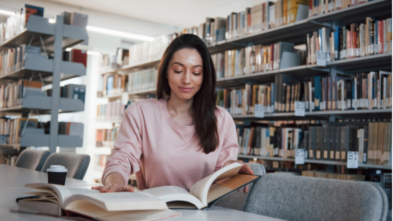 girl with brown hair reading a book in the library