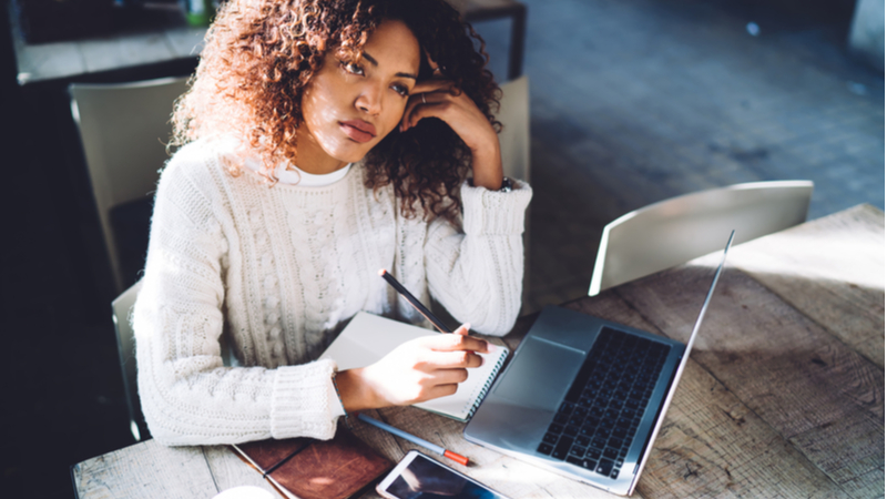 woman with curly hair thinking while studying with her laptop