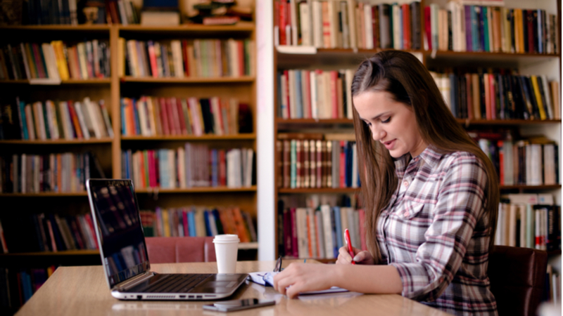 woman taking notes from her laptop in a library