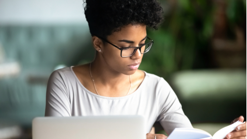 african american woman with short curly hair reading notes next to her laptop