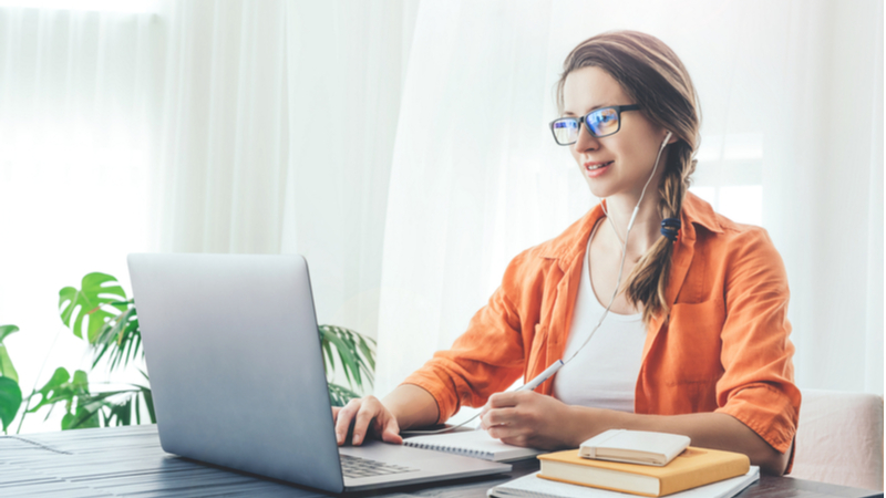 woman in orange jacket wearing headphones and working on her dissertation defense