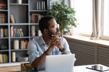 african american man contemplating and looking out the window in his home office