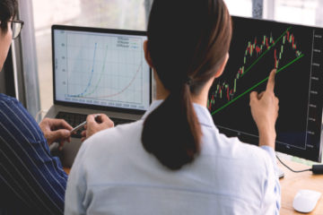 two people analyzing charts on their computers