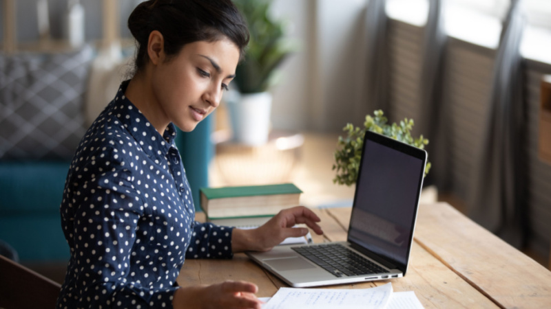 indian woman comparing notes between laptop and notepad