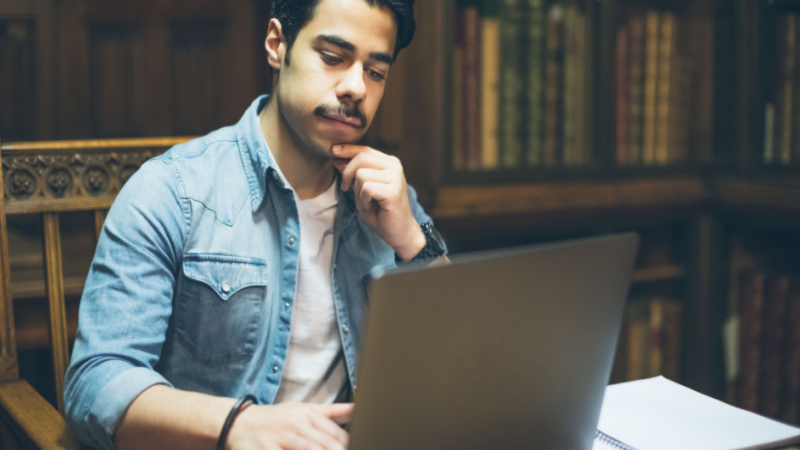 young man with mustache working on his dissertation at the library