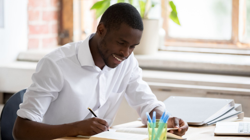 african american man smilingly writing in his notebook