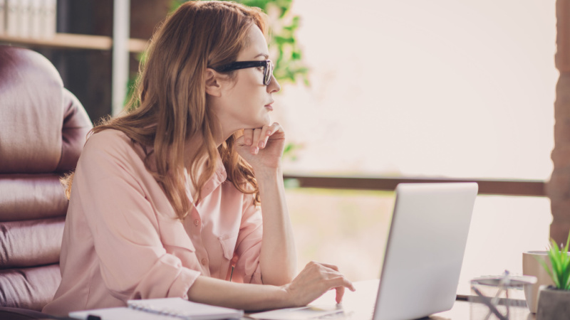 concentrated woman with glasses writing on her laptop