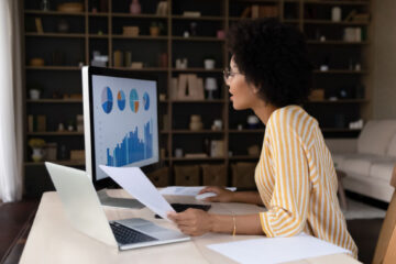 woman with curly hair comparing notes in front of computer