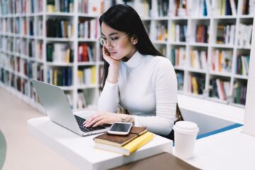 asian phd student researching on laptop in the library